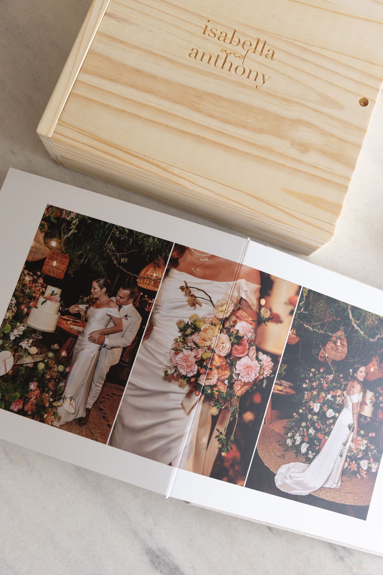 Wooden box with engraved names Isabella and Anthony above wedding photo album.