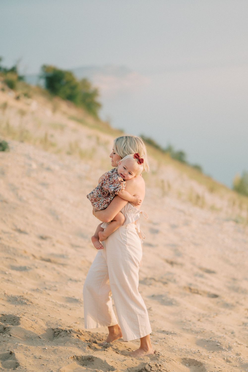 Parent and child share a tender moment on sandy beach dunes at sunset.