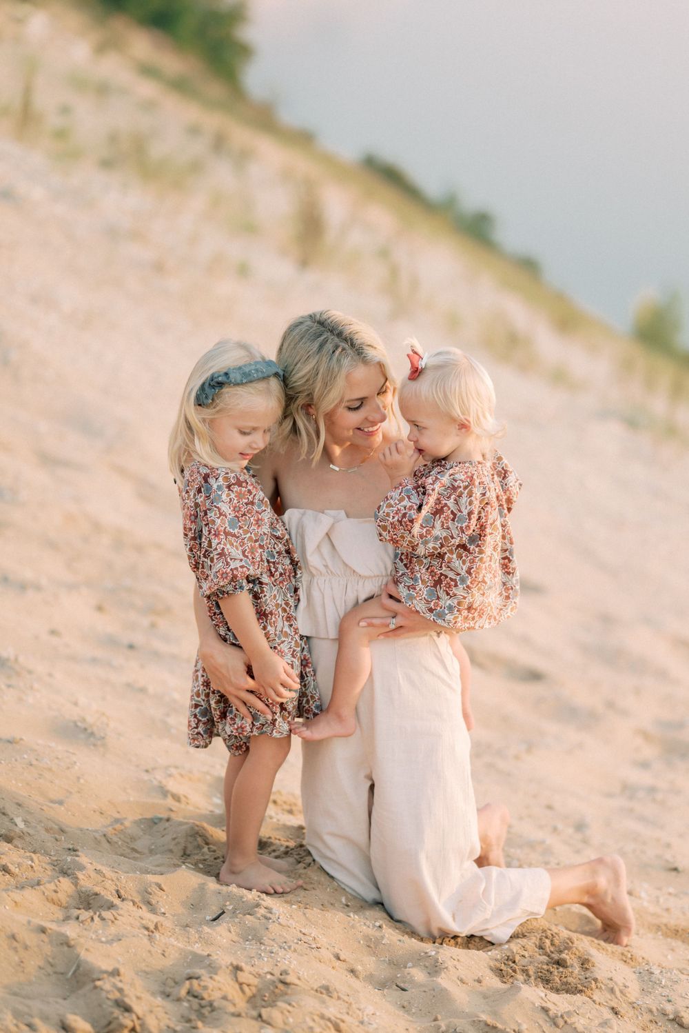Family shares intimate moment together on sandy beach hill during golden hour.