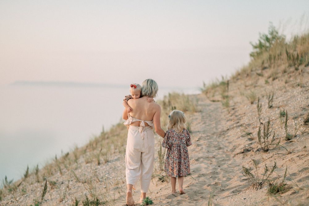 People walking along scenic coastal sand dunes at sunset.