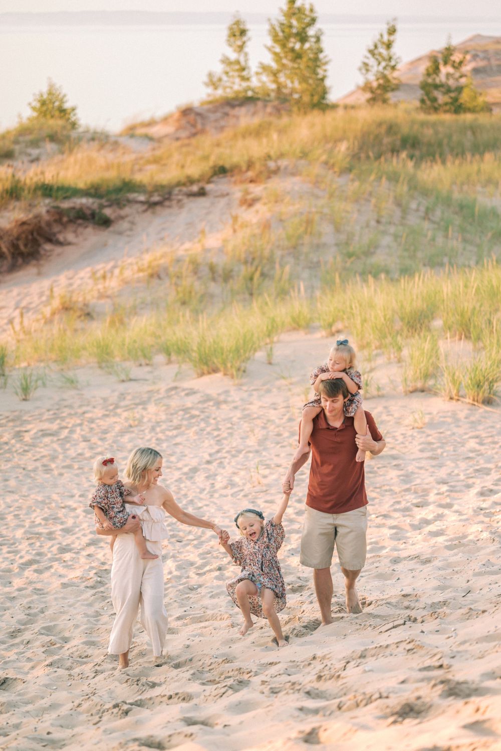Family playing together on sandy beach dunes during golden sunset.