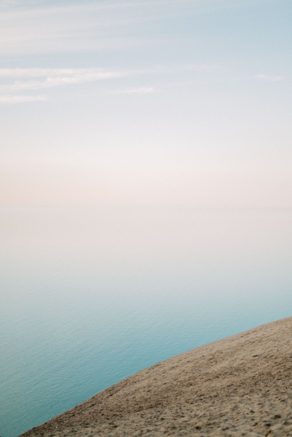Peaceful coastal landscape with turquoise waters meeting sandy cliffs under soft sky.