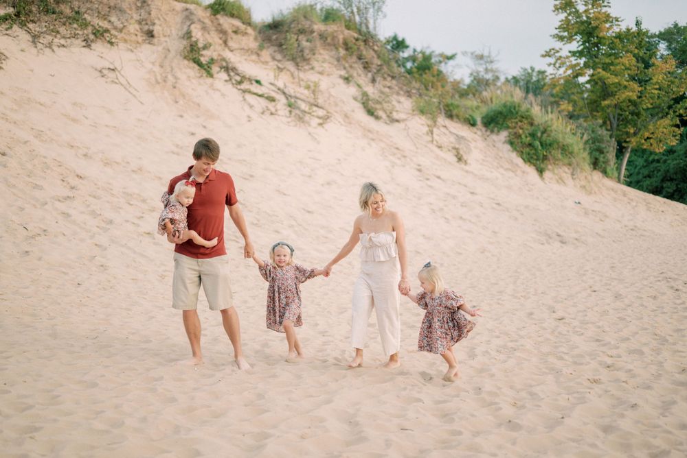 Family walking hand in hand up steep sandy dune path during golden hour.