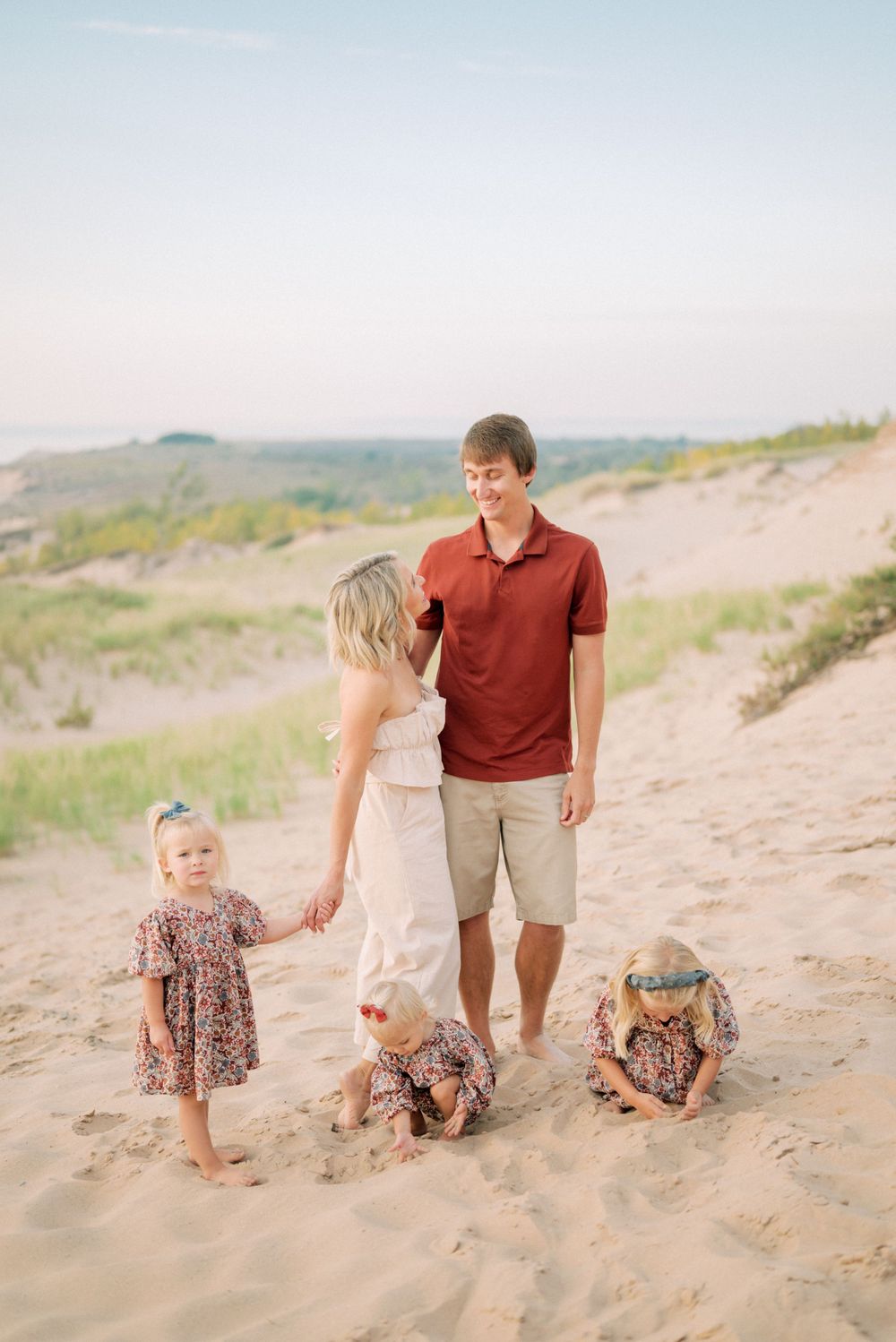 Family enjoying time together on sandy beach dunes during sunset.