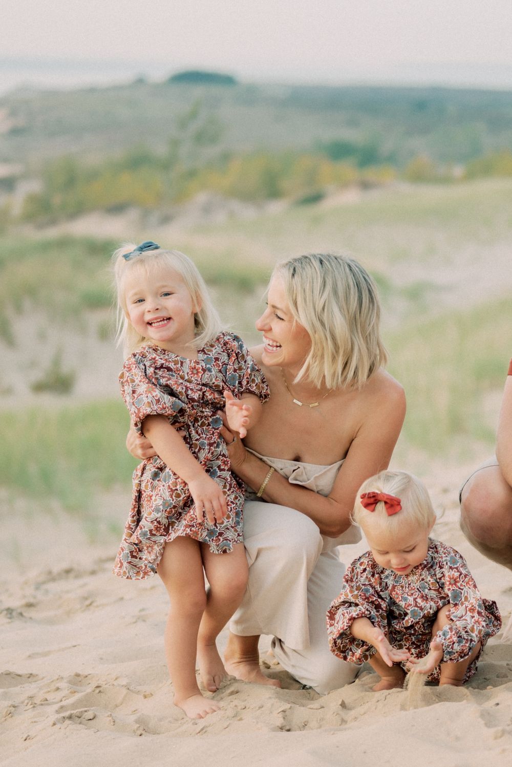 Parent and children in matching outfits playing together on sandy hillside.