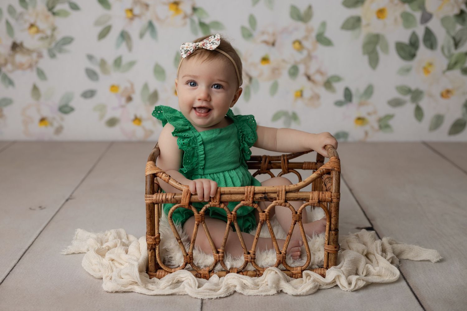 Nine month old baby girl in green sitting in a cute basket with a floral backdrop for her studio milestone portrait session.