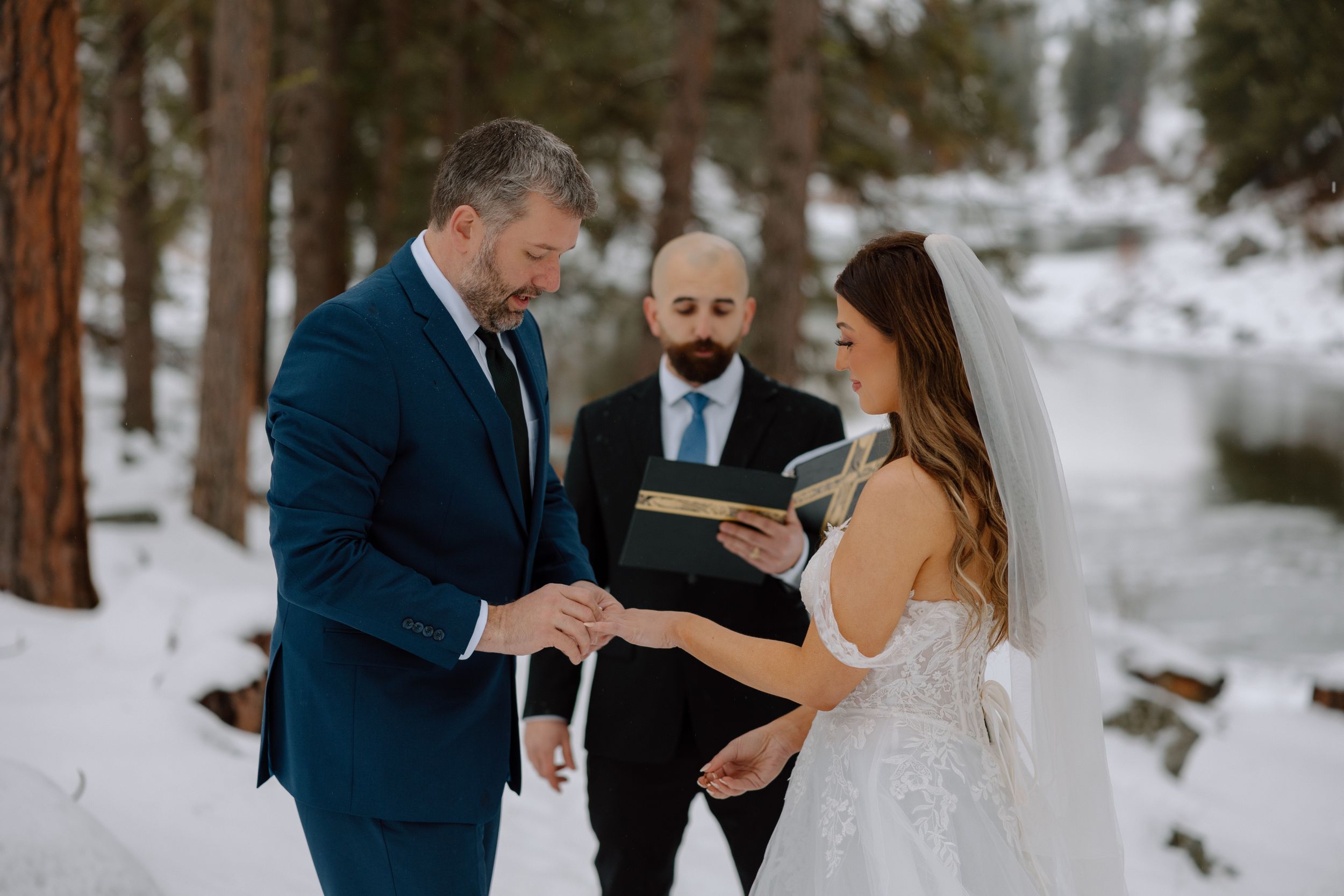 An intimate winter wedding ceremony takes place in a snow-covered forest setting.