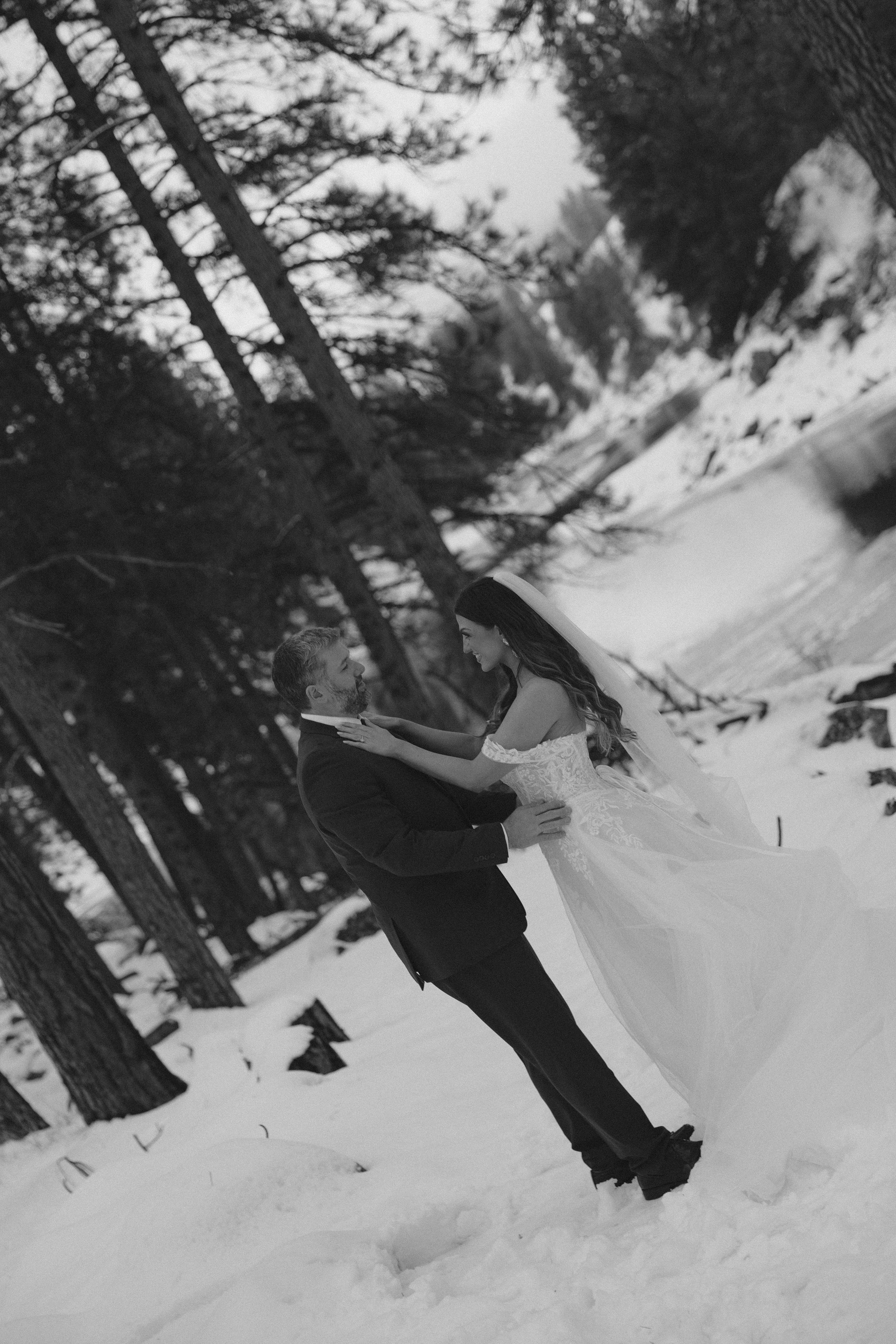 Two people dancing and twirling in a snowy forest setting, captured in black and white.