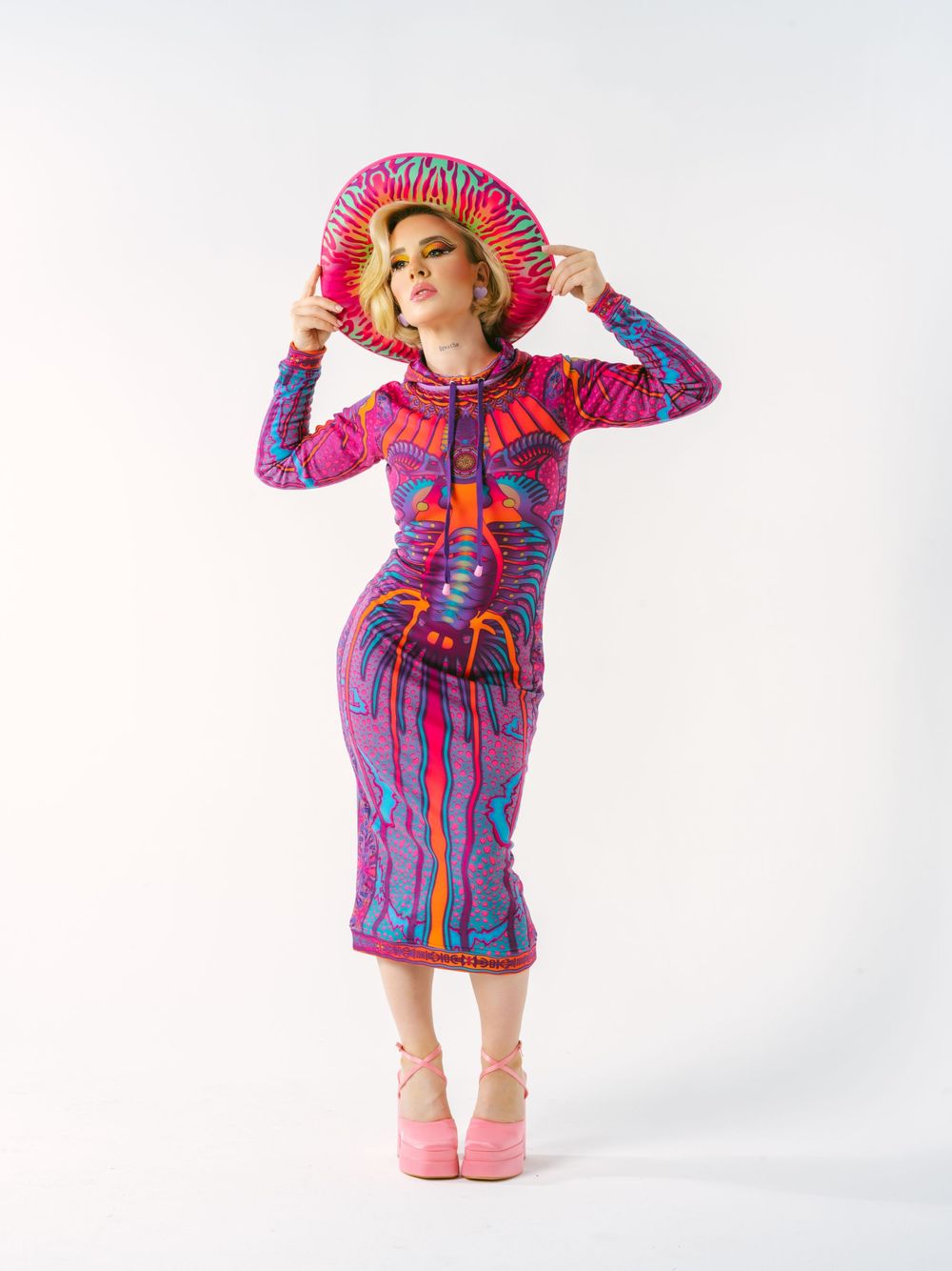 Fashion model in form-fitting retro dress with matching hat striking a pose against white backdrop.