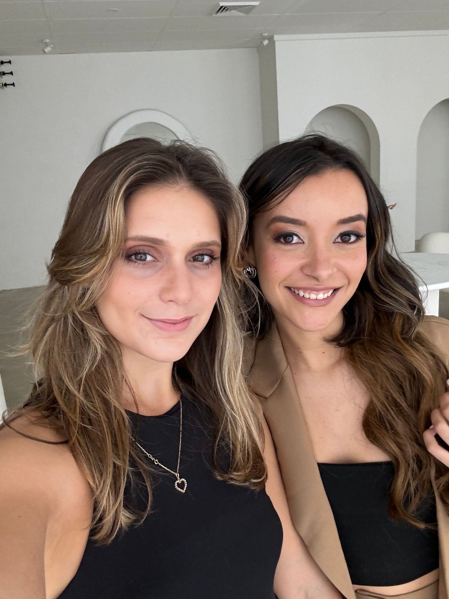 Two friends in black tops and blazers taking a casual selfie together indoors.