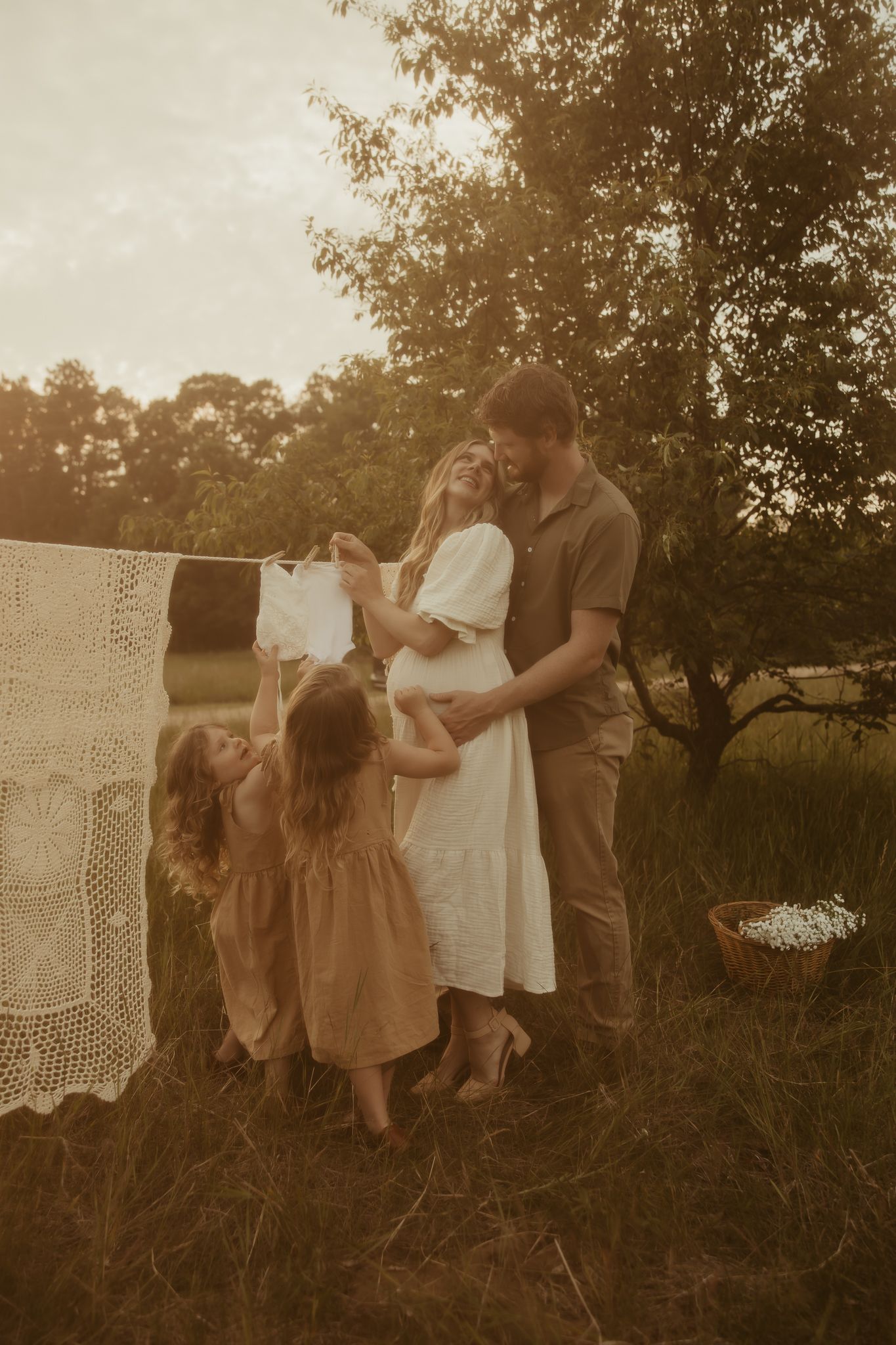 A warm-toned family portrait shows a tender moment of cuddling and affection against a neutral backdrop with dried florals.