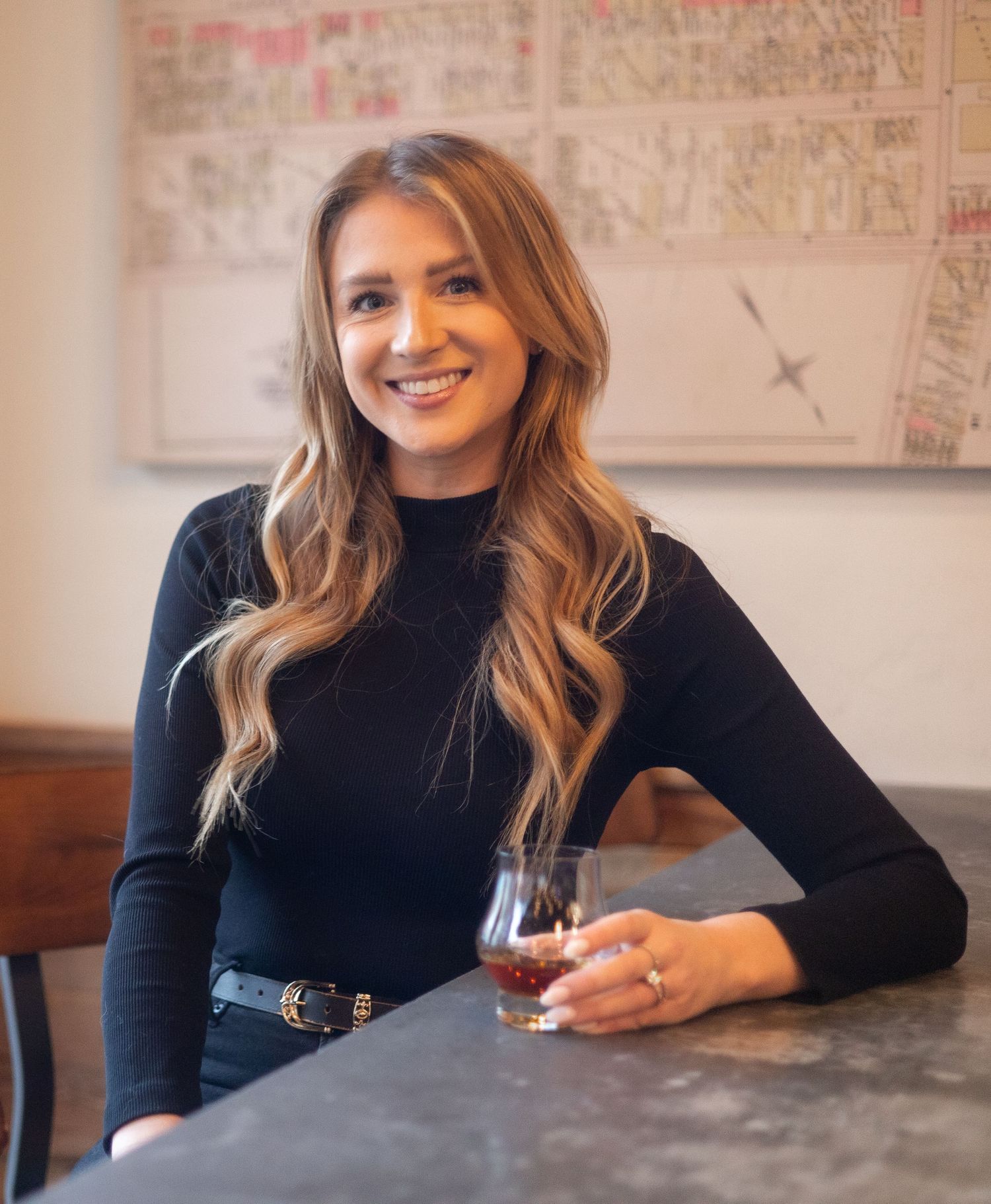 Woman in black sweater sitting at table with wine glass in modern setting.