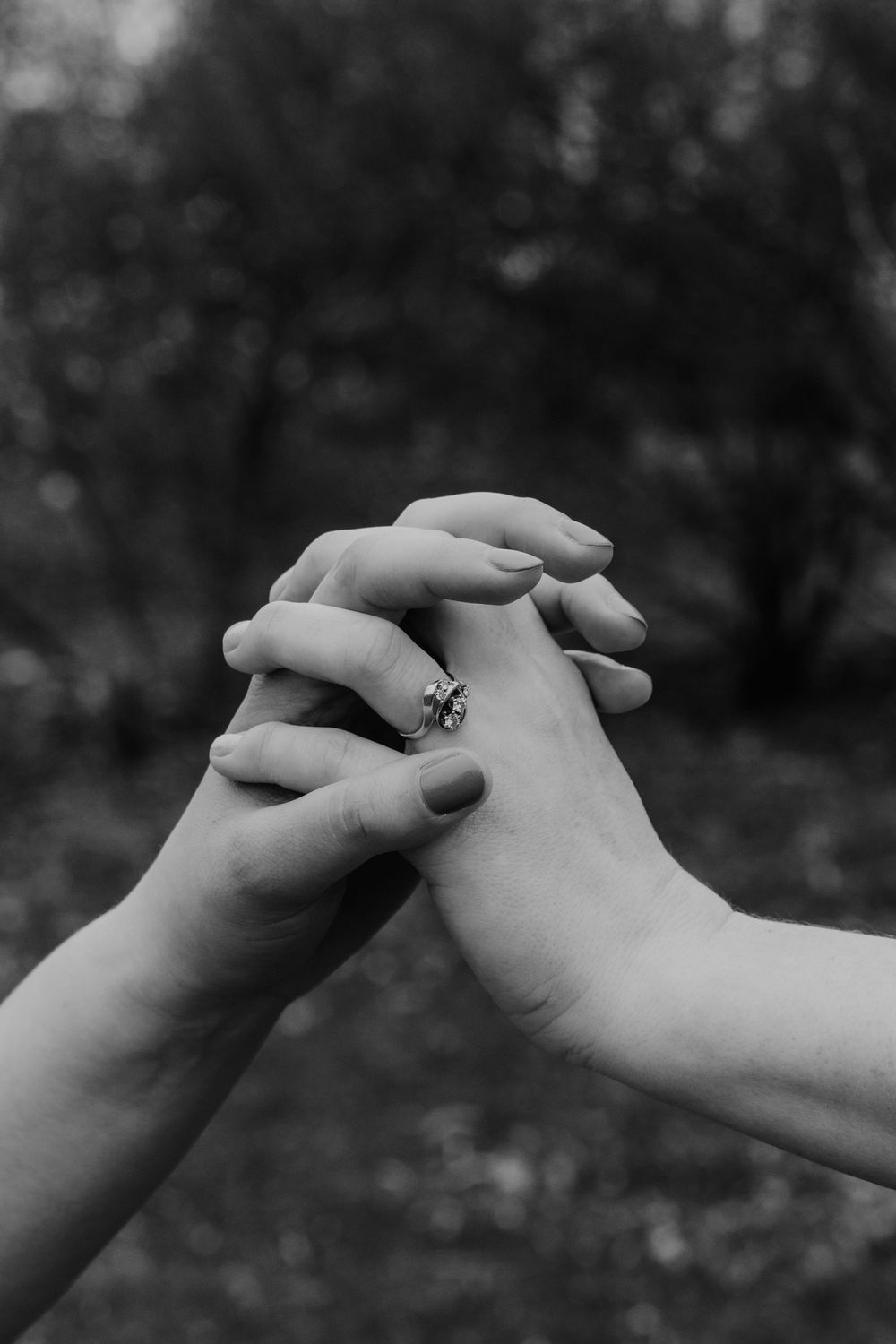 Two hands gently clasping in a tender moment against a blurred dark background, with one hand wearing a small ring.