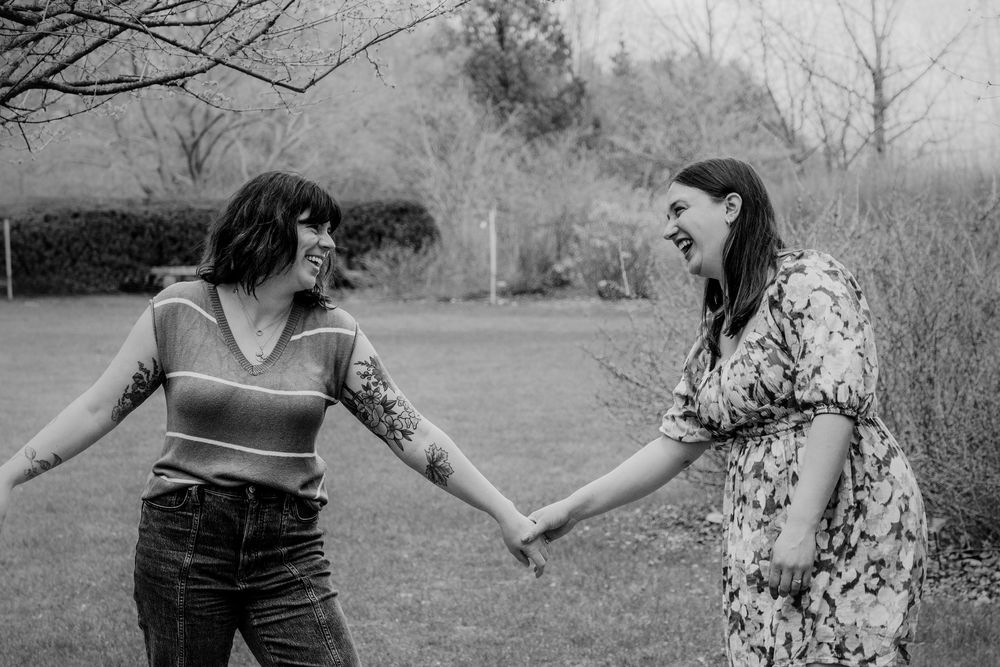 A black and white photo of two people holding hands and laughing together in a natural outdoor setting.