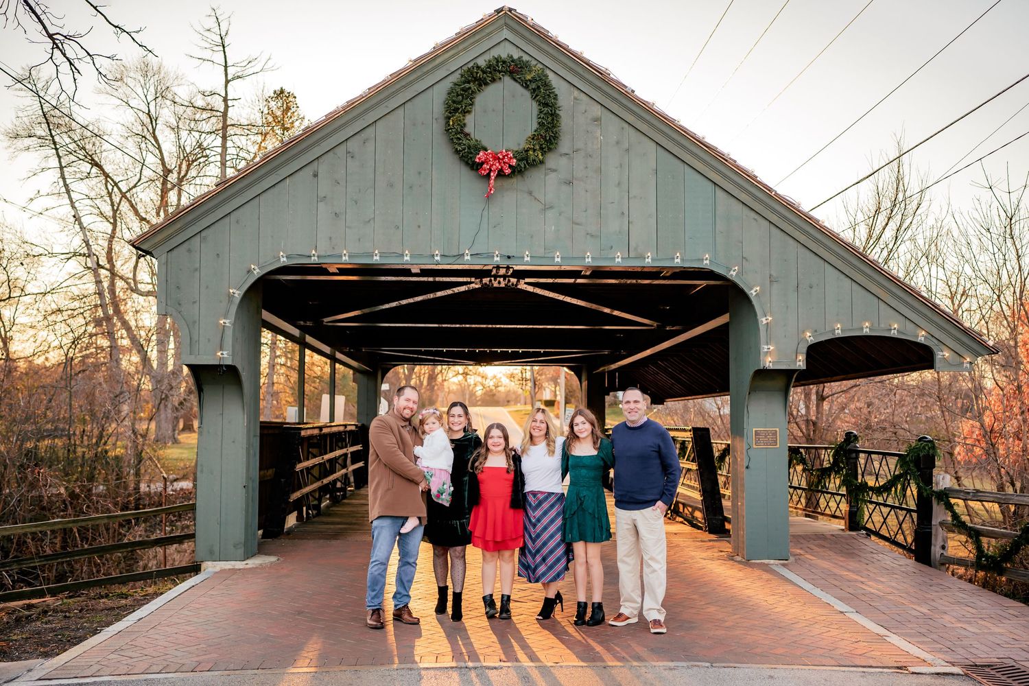 A family poses inside a covered bridge decorated with a Christmas wreath.