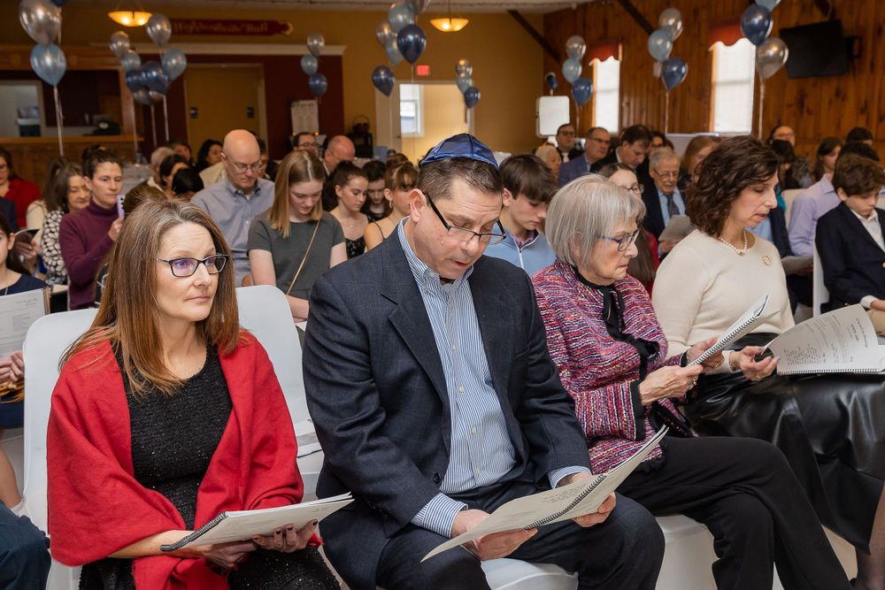 Audience members seated in rows at formal event with blue balloon decorations.