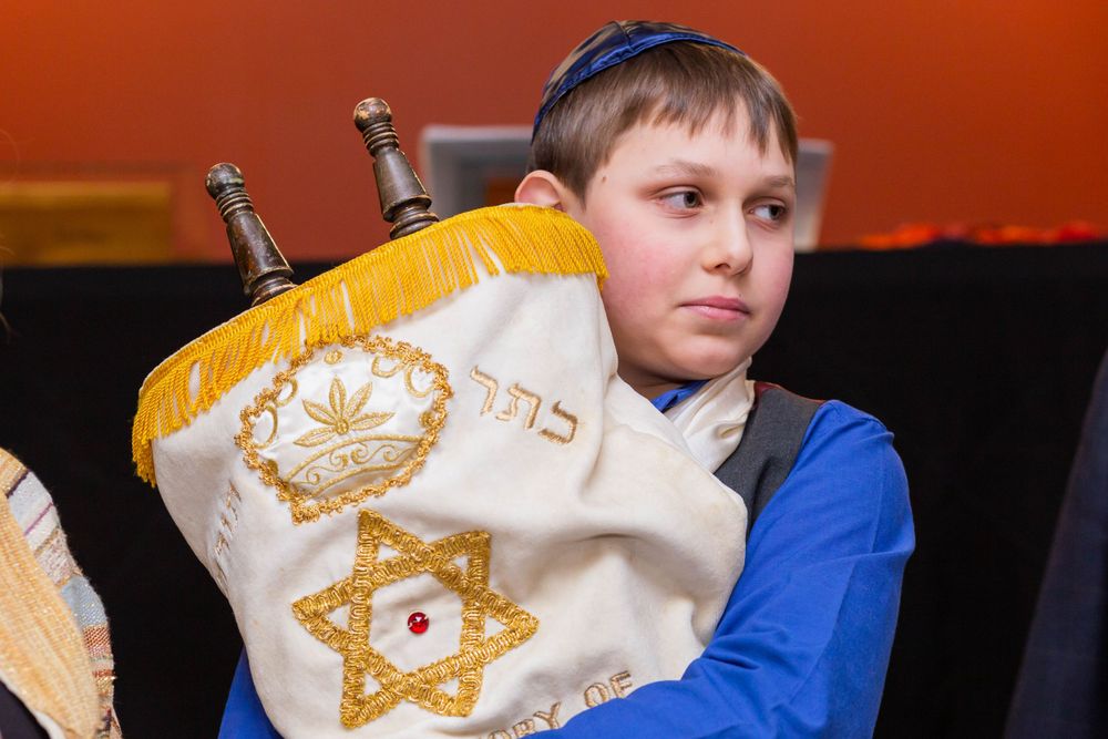 Young person in blue holding Torah scroll with decorative yellow cover featuring Star of David.