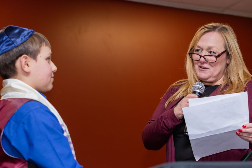 A young person in blue and white attire reads from a document during a religious ceremony.