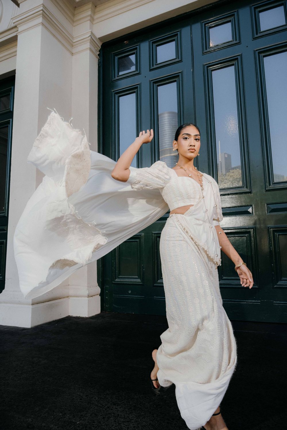 A flowing white vintage-style dress with billowing sleeves moves dramatically against a dark doorway background.
