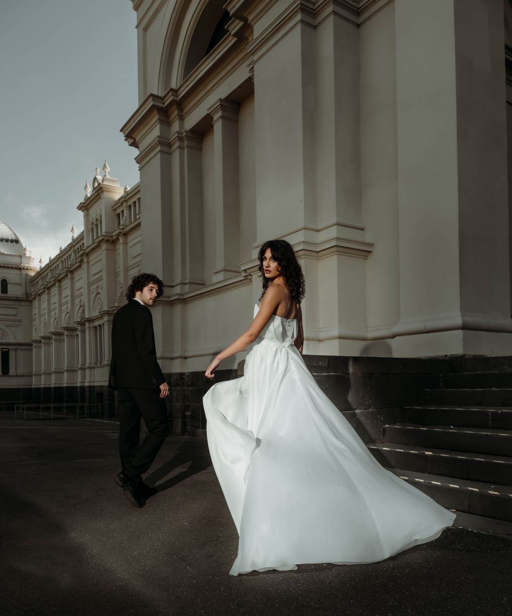 A couple in wedding attire dances gracefully on a grand staircase in front of a neoclassical building.