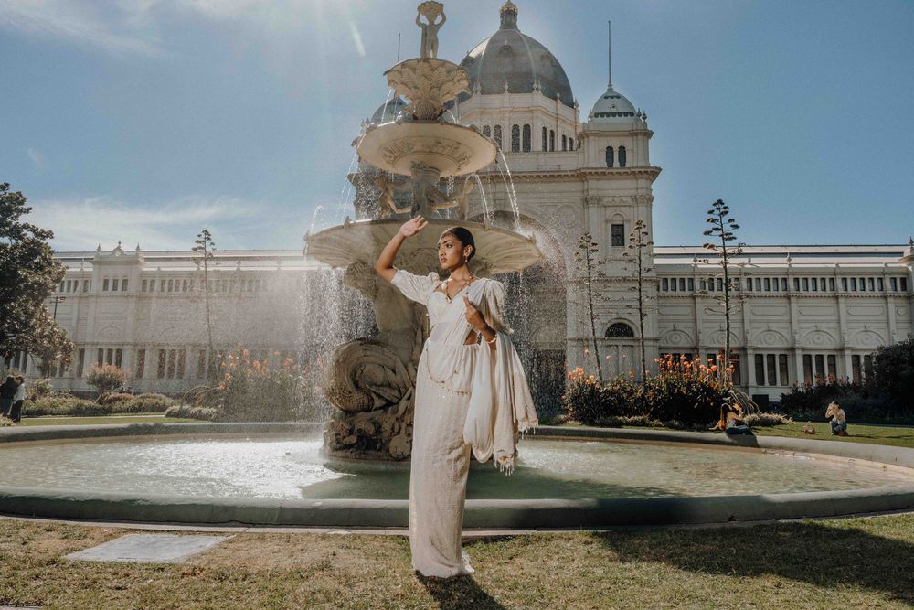 A person in a white dress poses in front of the Royal Exhibition Building and fountain in Melbourne, Australia.