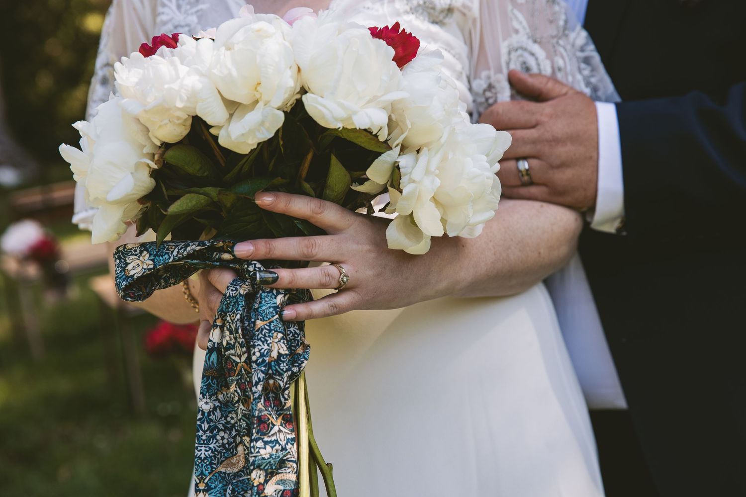 Elegant white and red wedding bouquet with blue patterned ribbon detail.