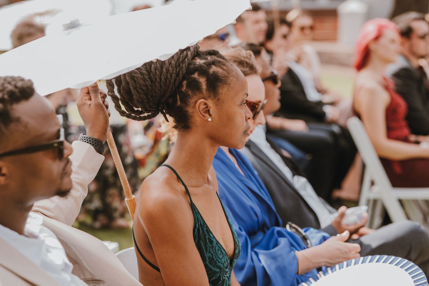 Wedding guests use handheld paper fans to stay cool during an outdoor summer ceremony.