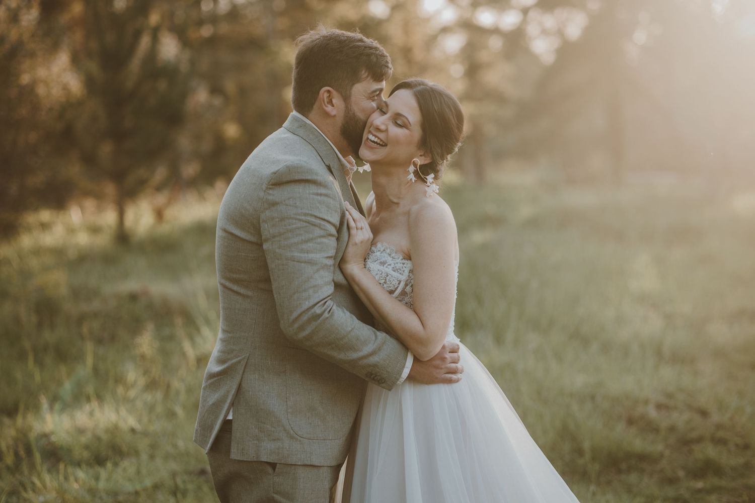 A tender wedding moment captured at golden hour with the couple embracing in a sunlit meadow.
