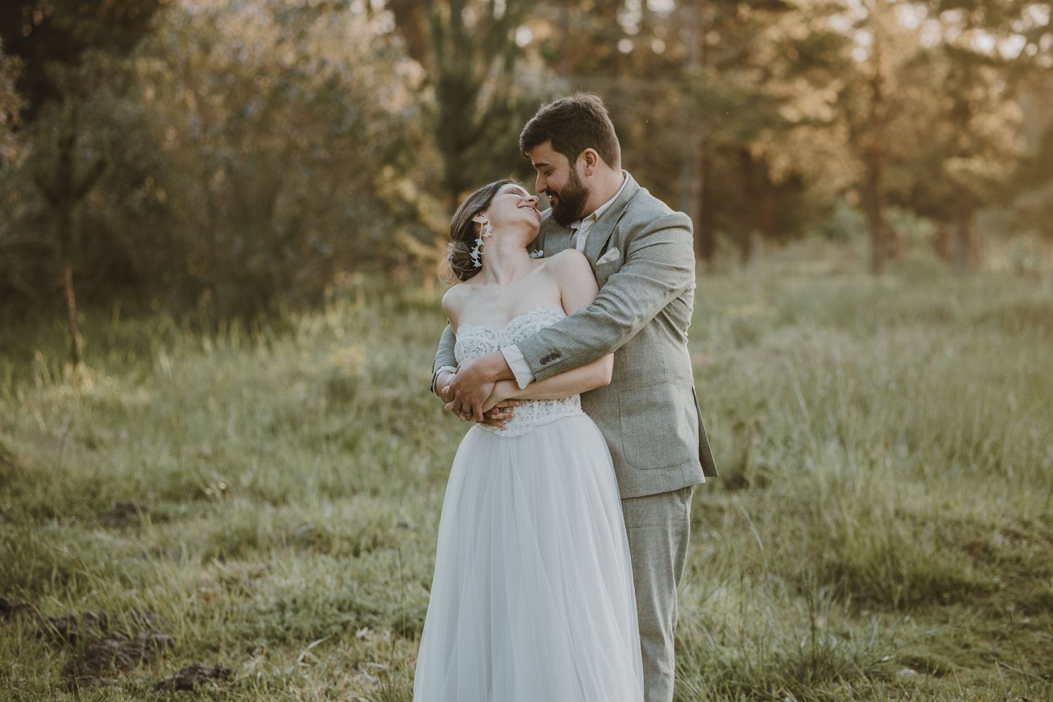 A romantic wedding couple embraces in a sunlit meadow at golden hour during a rustic outdoor ceremony.