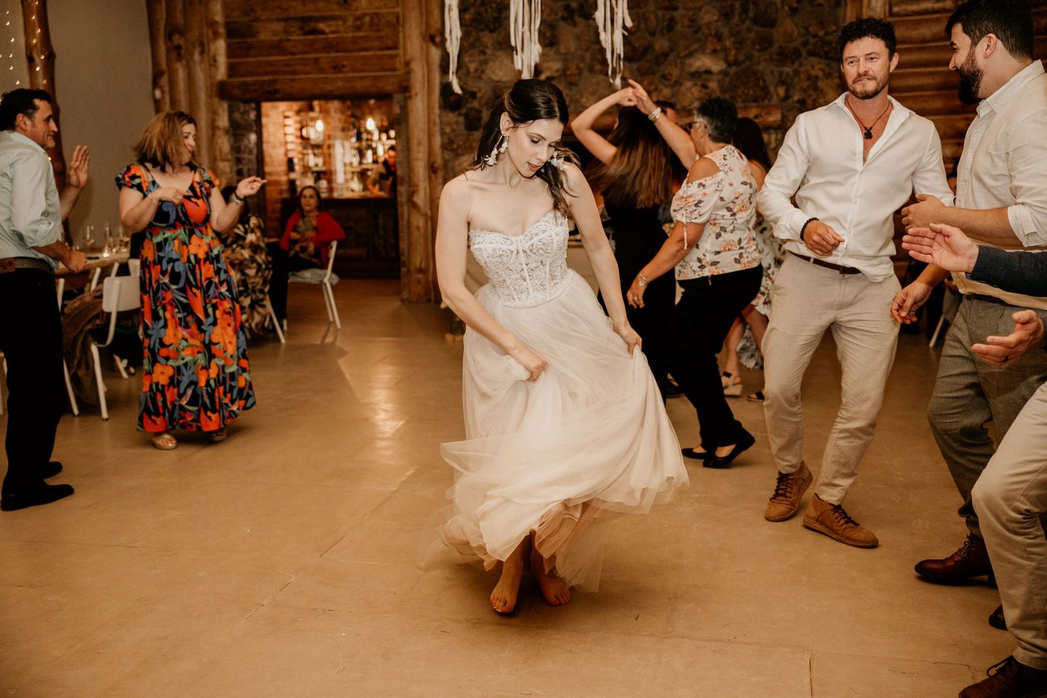 Wedding guests dance joyfully on a rustic indoor dance floor during a reception celebration.