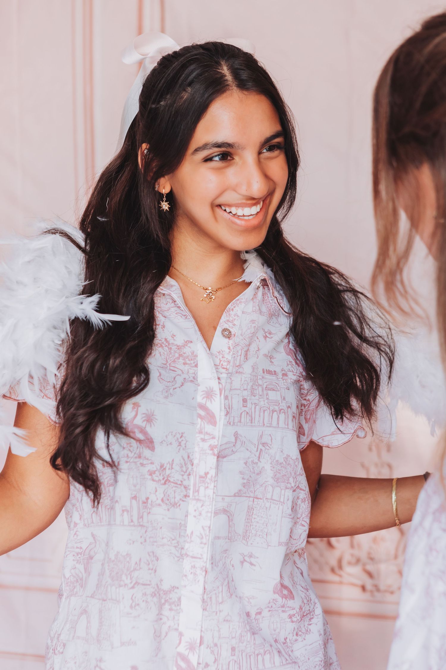 Woman wearing a delicate white and pink patterned blouse in a soft pink room.