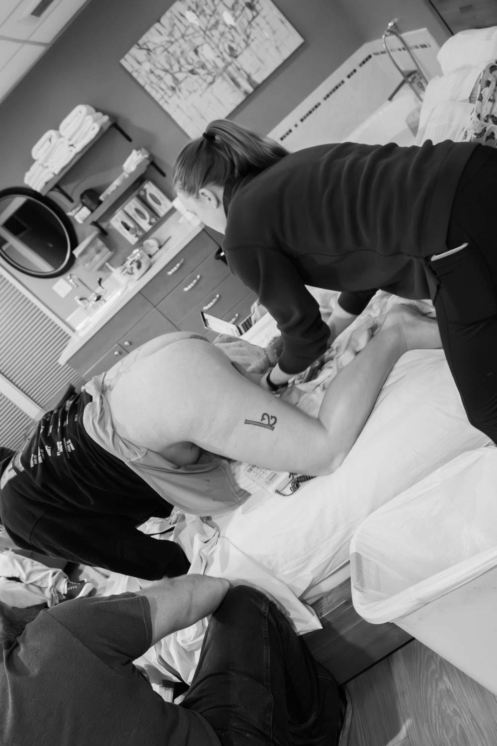 Black and white photograph showing a birthing assistant providing care and support during labor.