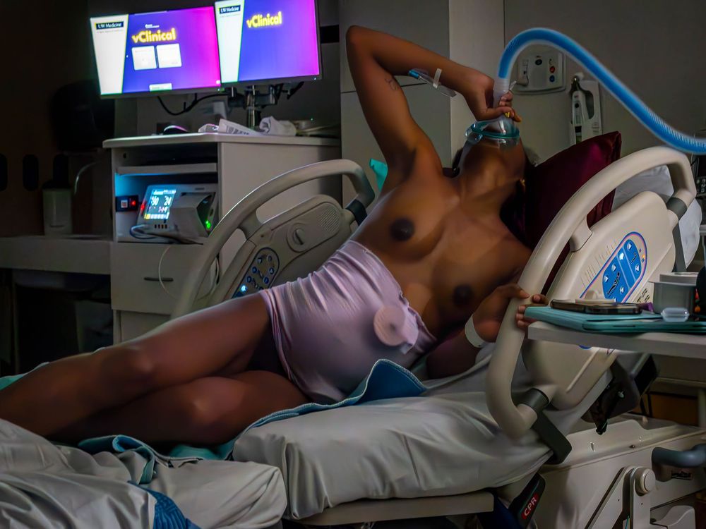 A mother labors in a hospital bed with medical equipment visible in the background.