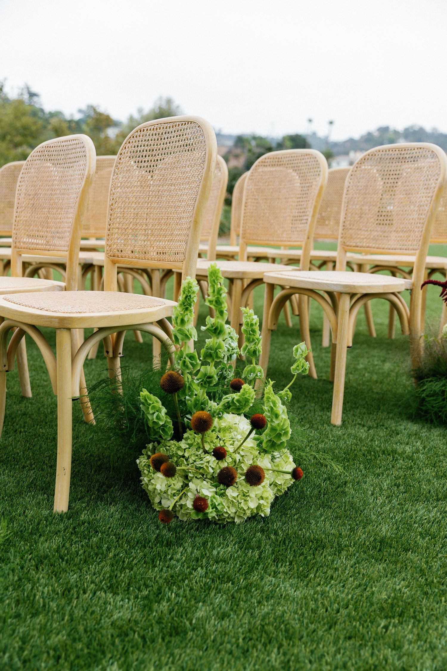 Vintage cane-back chairs arranged outdoors on grass with floral arrangement featuring sunflowers and greenery.