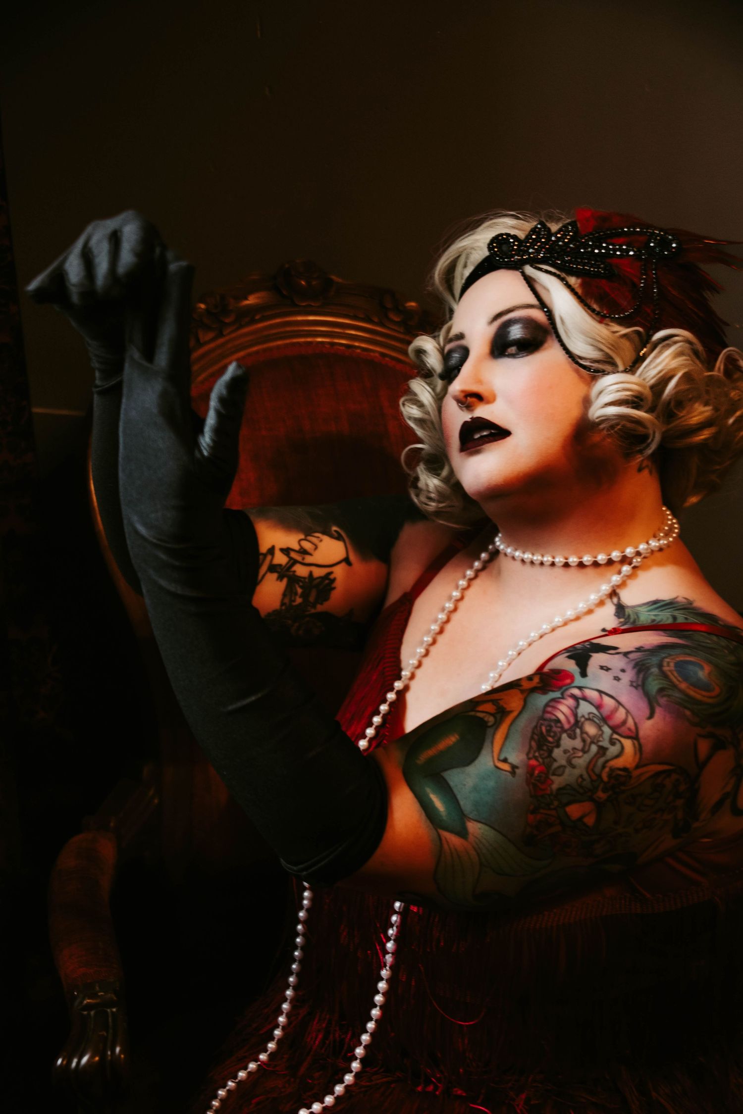 Dramatic vintage-style portrait featuring pearls, long black gloves, and 1920s-inspired makeup and hairstyle with dark lighting.