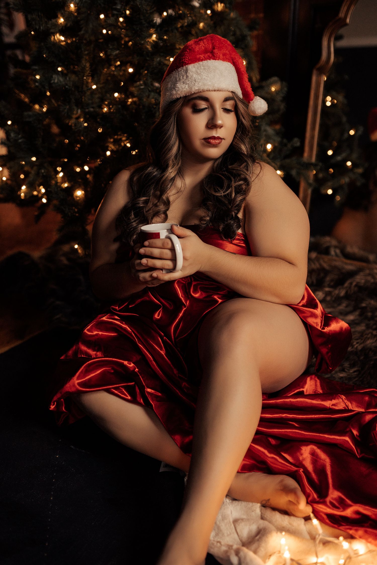 Festive holiday boudoir photo with Christmas tree lights and red satin fabric.