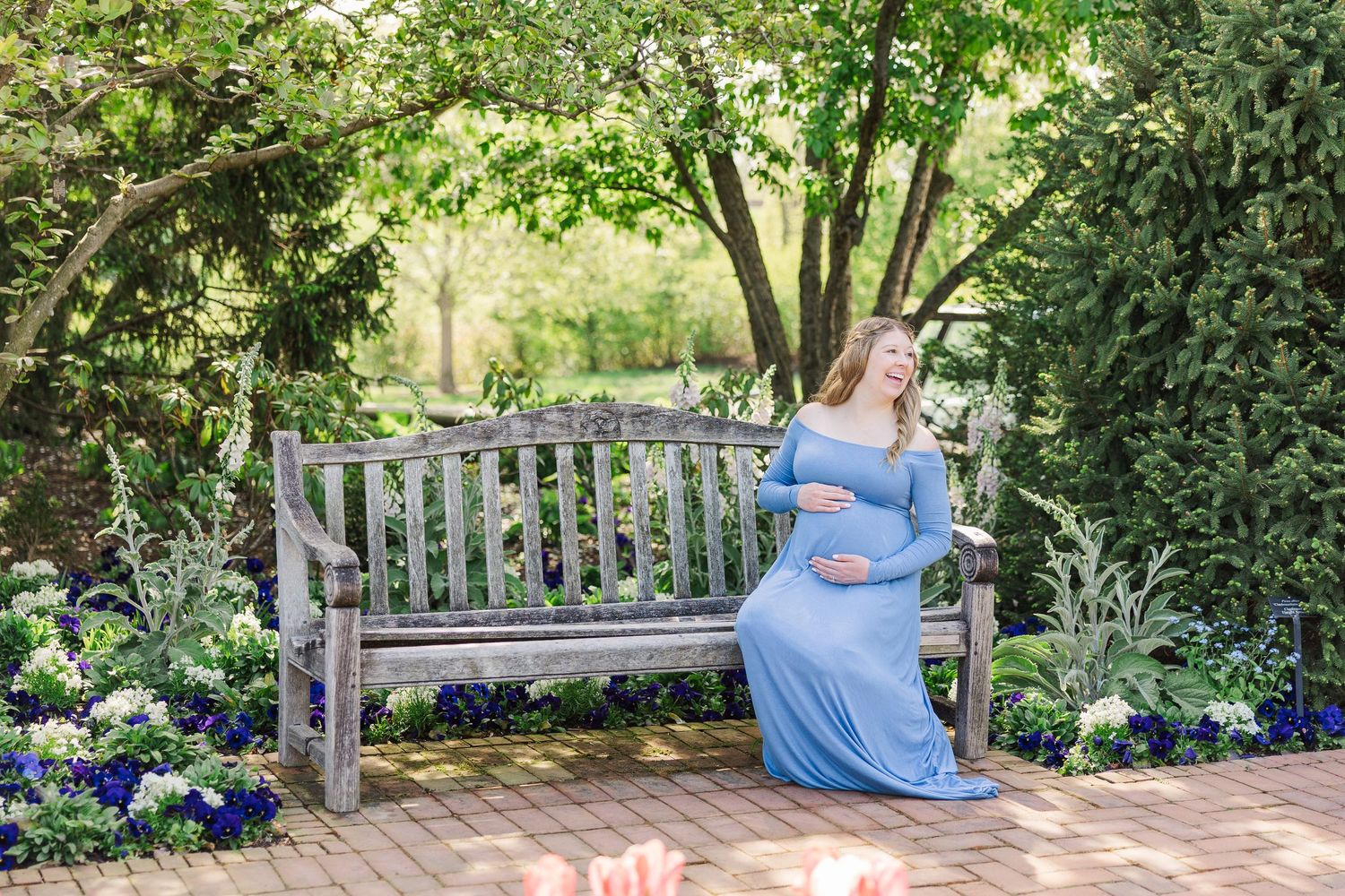A person in a flowing blue dress sits on a wooden garden bench surrounded by blooming flowers and lush greenery at Chicago Botanic Garden