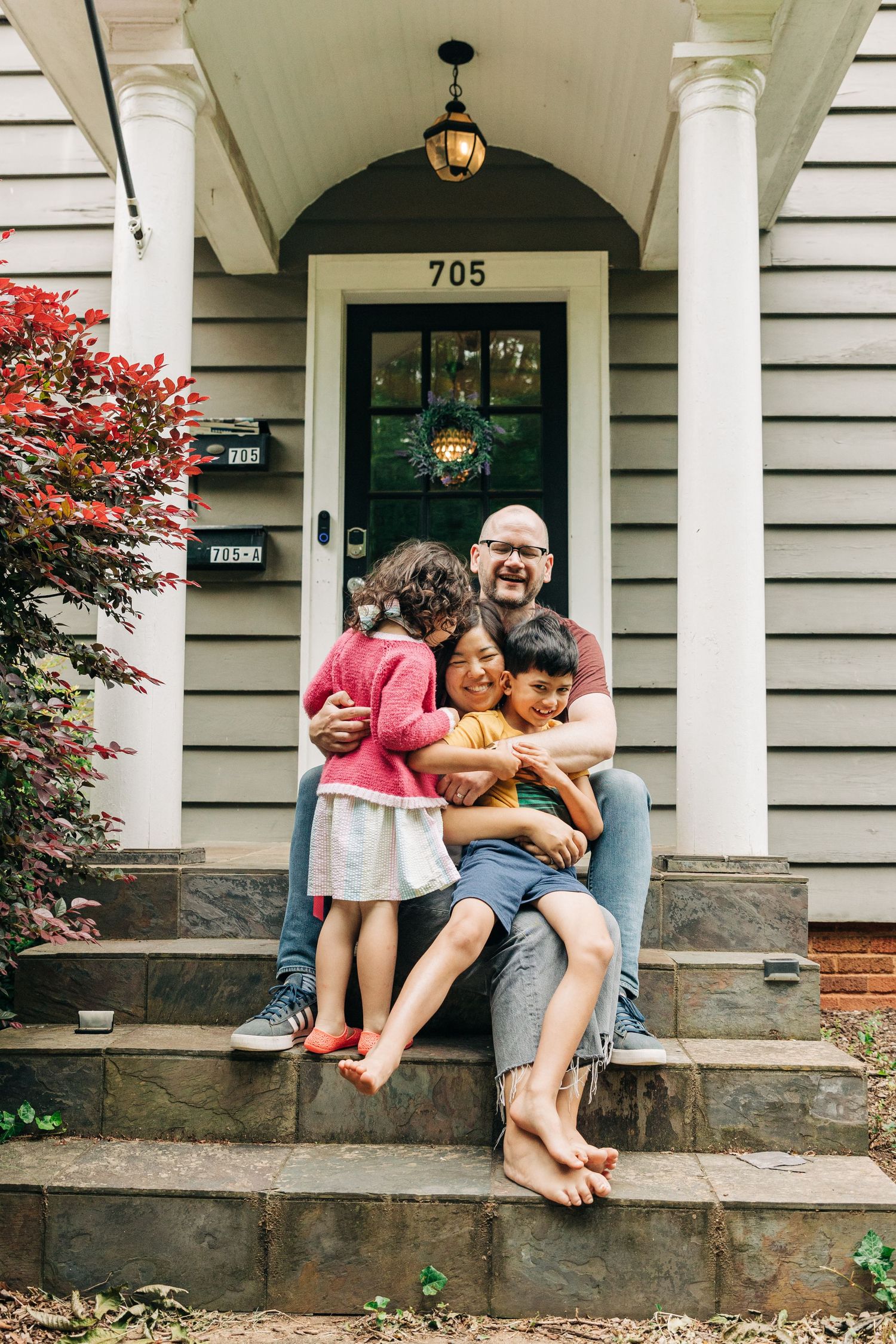 A cozy front porch scene of a family with brick steps, white columns, and a dark door under a hanging lantern in Charlotte, NC