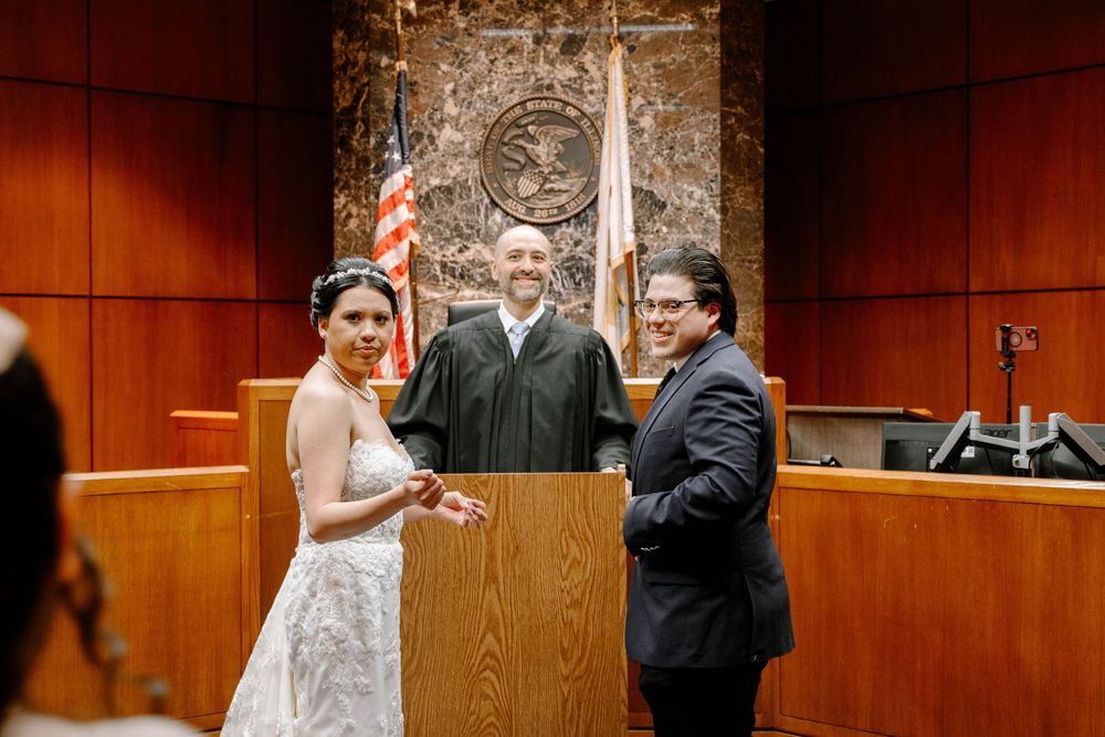 A civil ceremony takes place in a courtroom with a judge presiding over a couple exchanging vows.