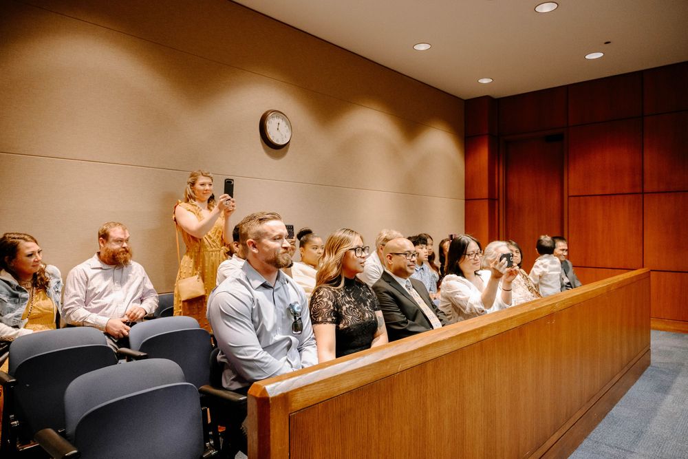 Wedding guests seated in courtroom benches watching an emotional ceremony unfold.
