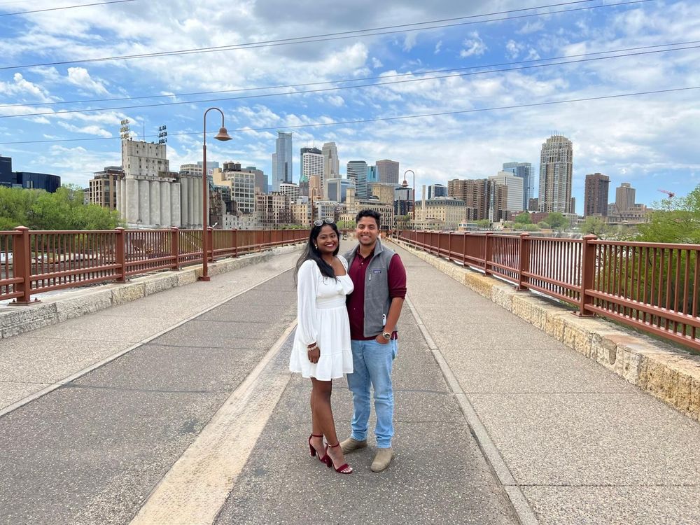 A couple poses on the Stone Arch Bridge with the Minneapolis skyline in the background.