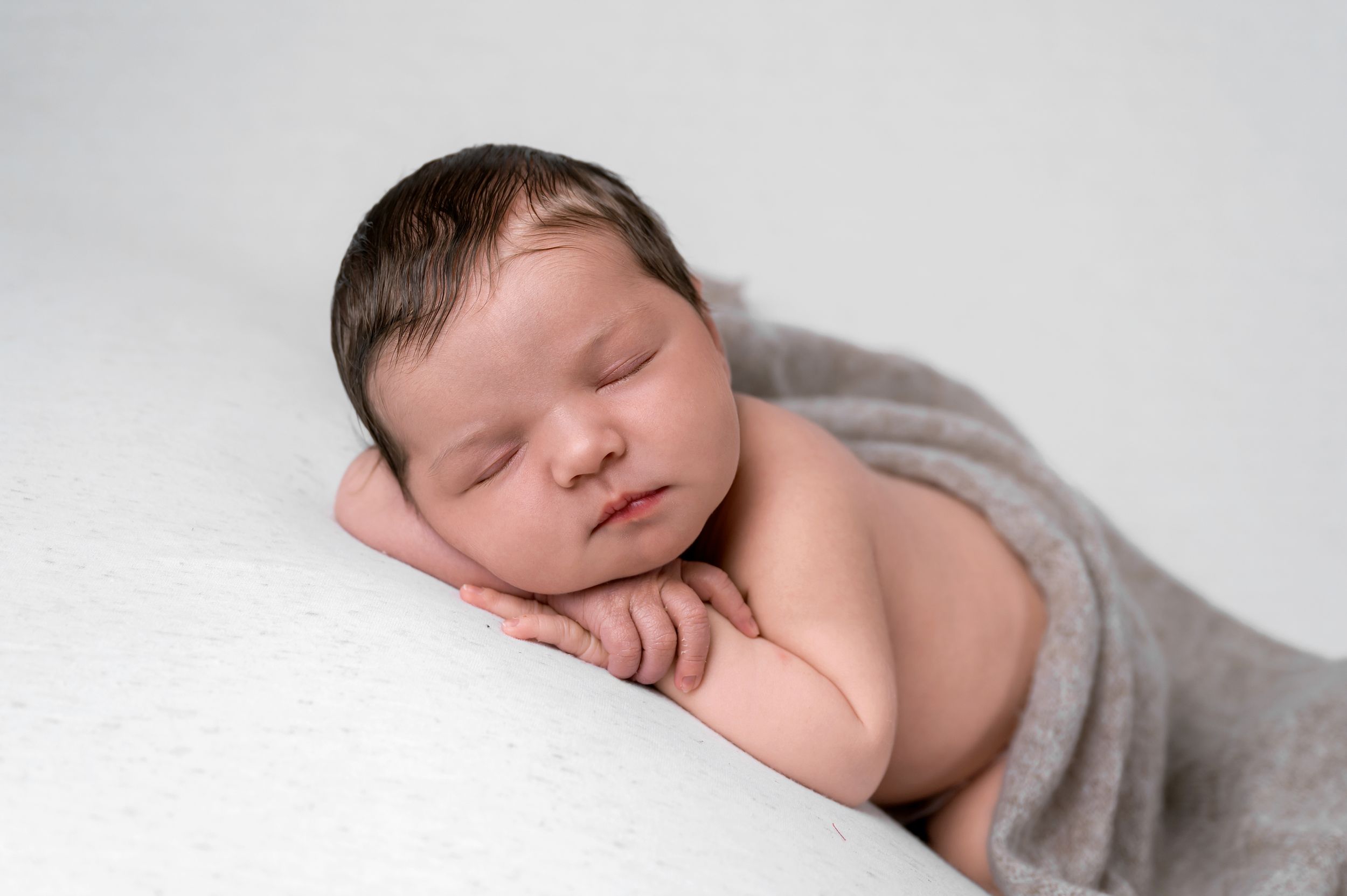 Peaceful sleeping newborn baby wrapped in soft gray blanket lying on white background during professional photoshoot.