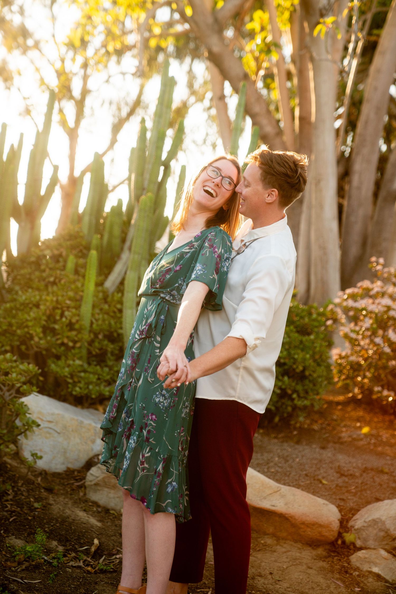 A couple shares a joyful moment together outdoors along a sunlit garden path on a warm afternoon.