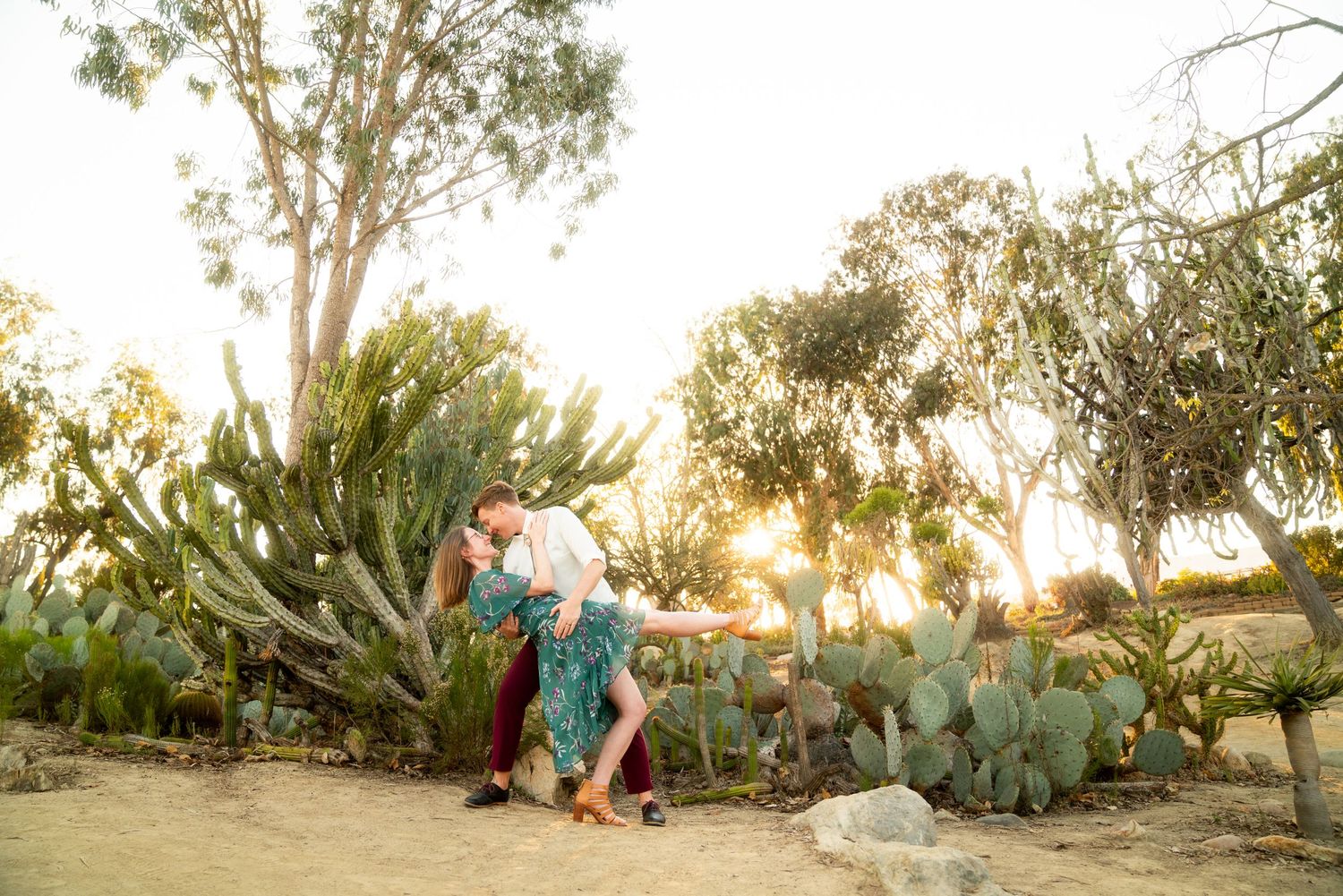 A couple dancing together at sunset among desert cactus and trees in a romantic garden setting.