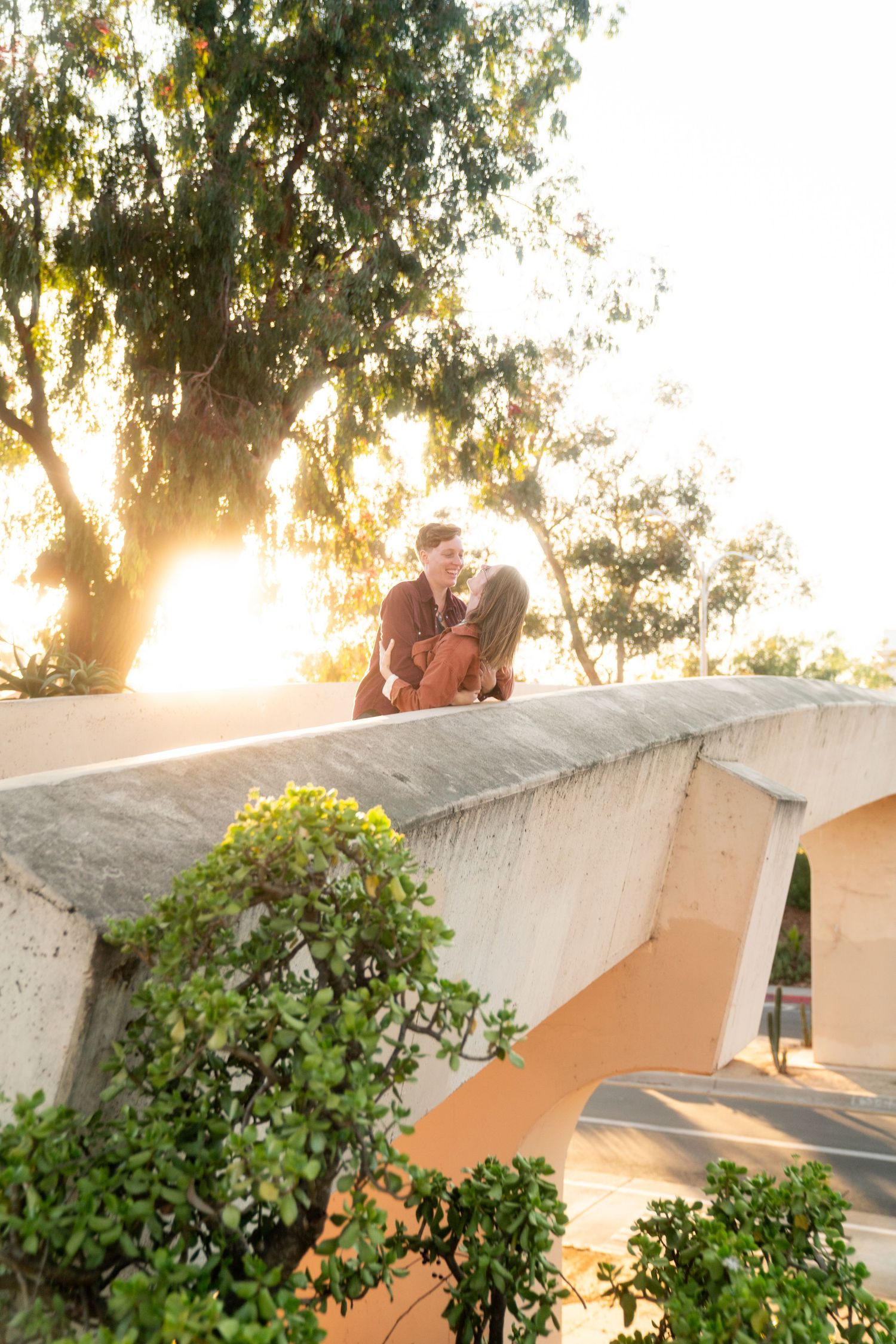 A couple shares a romantic moment at sunset against architectural arches and lush greenery.