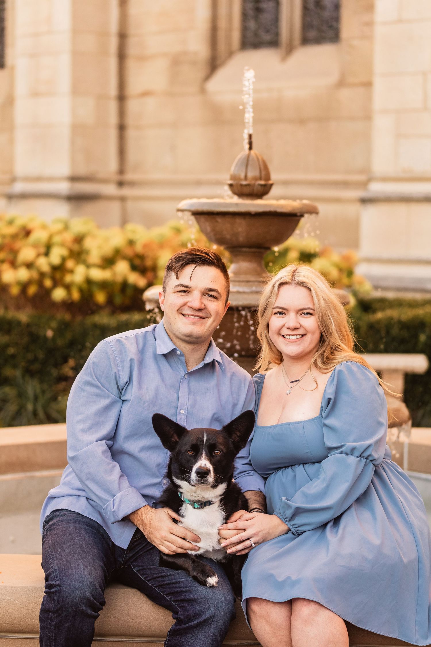 A couple wearing coordinating blue outfits sits outdoors with their black and white border collie dog on stone steps.