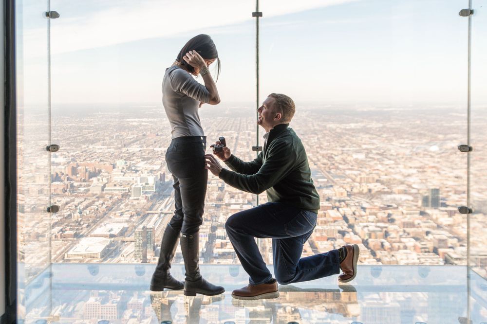 A marriage proposal takes place on a glass observation deck overlooking a vast cityscape below.