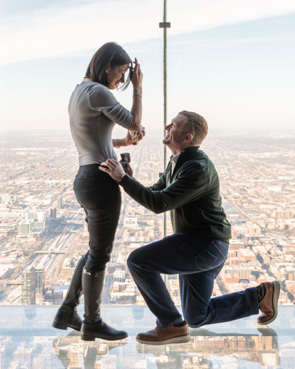 A marriage proposal scene with two people on a glass observation deck overlooking a cityscape below.