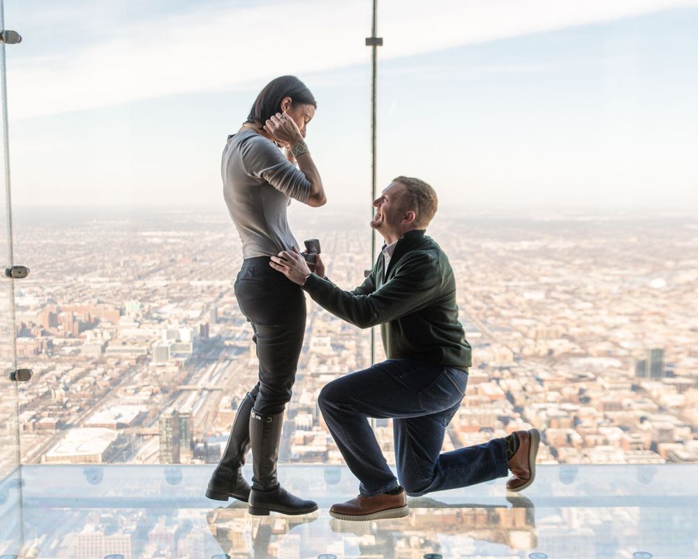 Proposal photo on a glass skydeck observation platform overlooking a vast cityscape below.