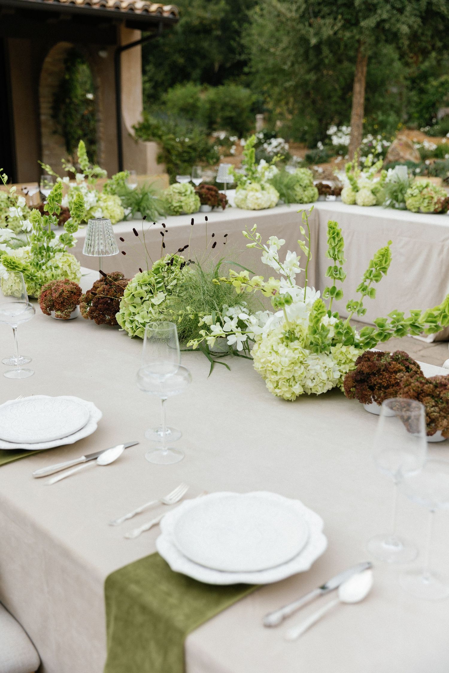 Elegant tablescape with white and green hydrangea centerpieces on linen tablecloth with place settings.